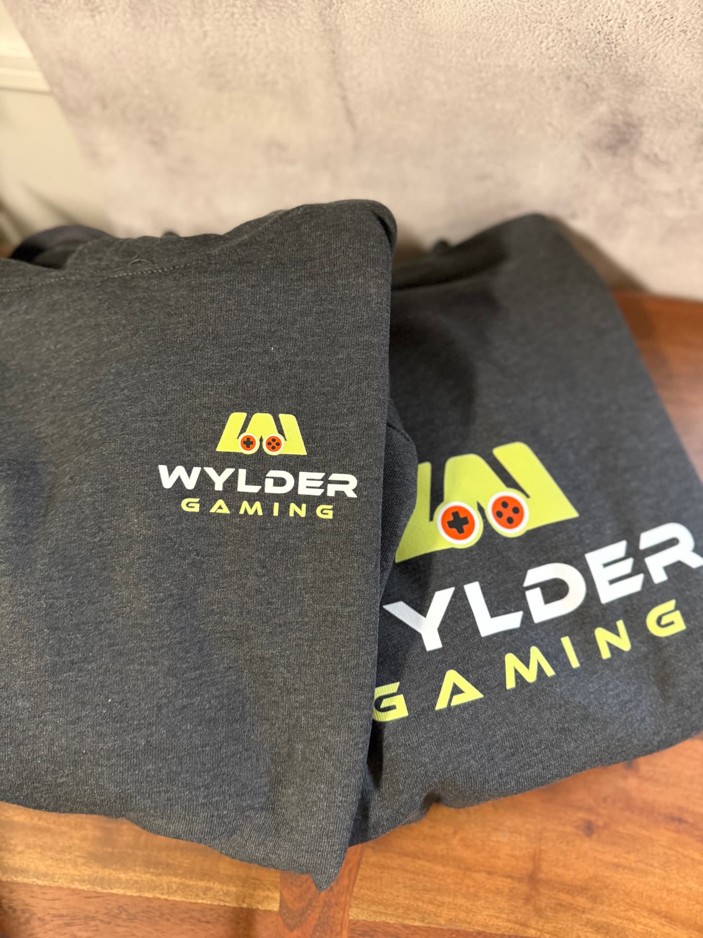 Two charcoal Wylder Gaming hoodies with green and orange controller logo prints